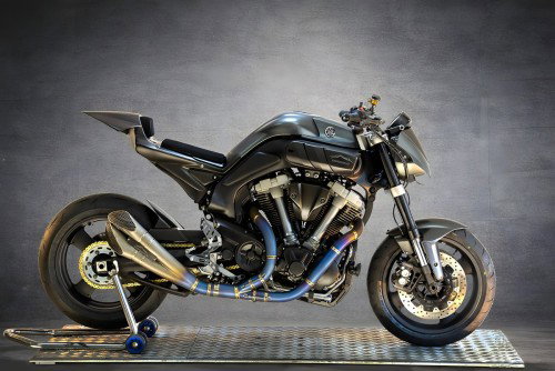 Yamaha MT-01 ORCO – Seitenansicht links auf Metallgitter im Studio, komplett umgebauter Streetfighter mit Karbonfaser-Verkleidung, goldener Auspuffanlage und blauem Montageständer