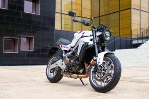 Yamaha XSR900 2027 – schräge Frontansicht in Neon White vor modernem Gebäude mit goldener Glasfassade