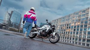 Yamaha XSR900 2027 – Fahrer geht zur geparkten XSR900 in Neon White auf einer Brücke zwischen Glasfassaden