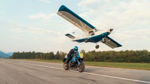 Yamaha XSR900 GP 2027 – Fahraufnahme in Legend Blue auf einer Flugplatz-Piste, darüber ein startendes Kleinflugzeug