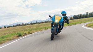 Yamaha XSR900 GP 2027 – Fahraufnahme in Legend Blue in einer Kurve, Frontansicht mit gelber Halbschale und LED-Scheinwerfer