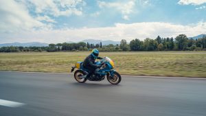 Yamaha XSR900 GP 2027 – Fahraufnahme in Legend Blue auf einer Piste mit Wiese und Bäumen im Hintergrund