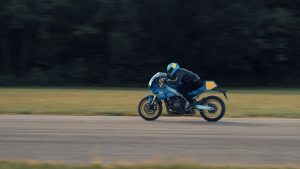 Yamaha XSR900 GP 2027 – Fahraufnahme in Legend Blue vor dunklem Waldrand mit Bewegungsunschärfe