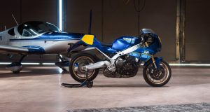 Yamaha XSR900 GP 2027 – Seitenansicht in Legend Blue auf Montageständer in einem Hangar neben einem Sportflugzeug