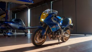 Yamaha XSR900 GP 2027 – schräge Frontansicht in Legend Blue im Hangar mit einfallendem Sonnenlicht
