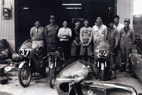 Historische Schwarzweißaufnahme: Team-Gruppenfoto vor der Yoshimura-Werkstatt mit Rennmotorrädern der Startnummern 37 und 52 (zeitgeschichtliches Pressefoto, Bildnachweis Yoshimura Japan)