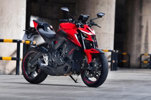 Zontes 703R 2027 - Lava Red, Actionaufnahme in einer Betonarchitektur-Kulisse mit Absperrgittern, Dreiviertelansicht von hinten